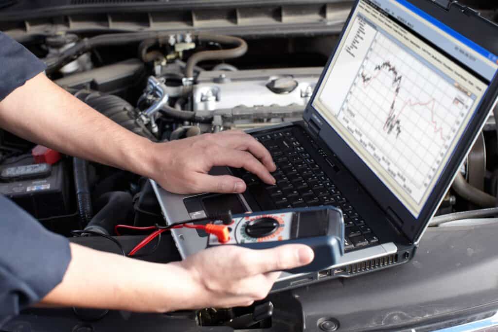 Technik s notebookem a měřicím přístrojem u otevřeného motorového prostoru